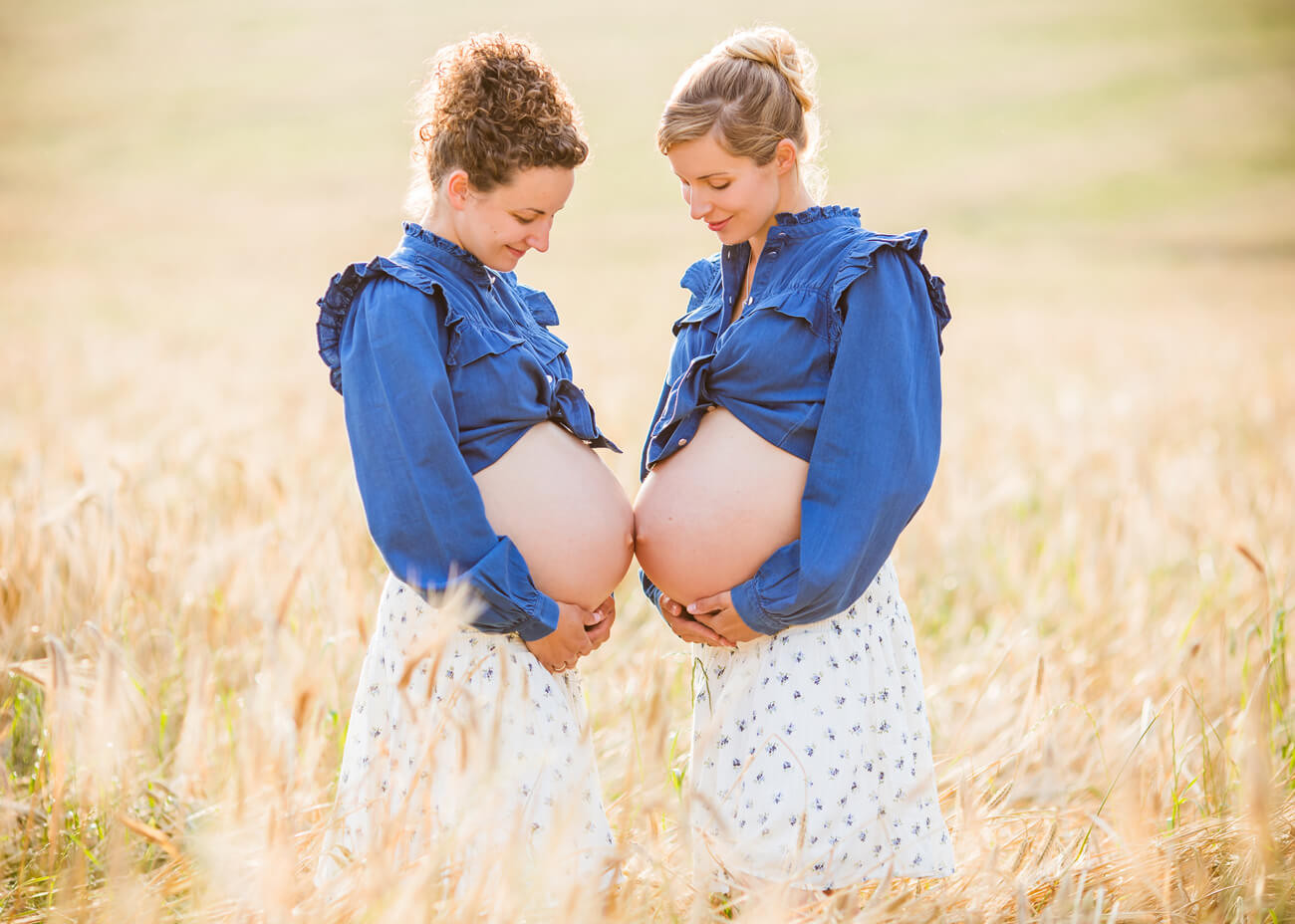 Schwangere Schwestern halten ihre Bäuche aneinander im Kornfeld, Outdoorbabybauchfotografie