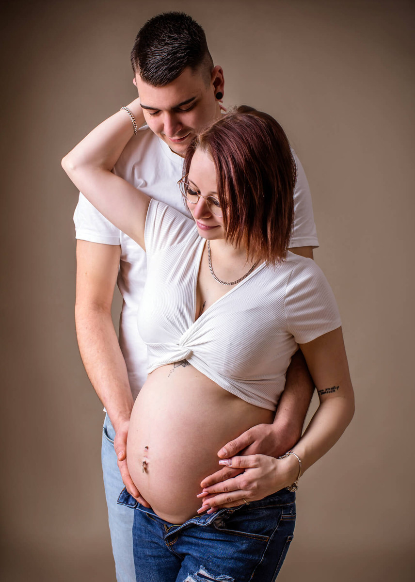 werdende Mama mit Mann dahinter schauen auf Babybauch 