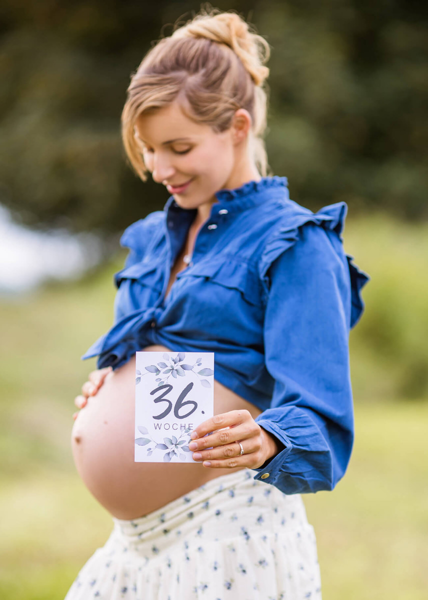 Schwangere hält Karte vor Babybauch mit der Aufschrift 36. Woche