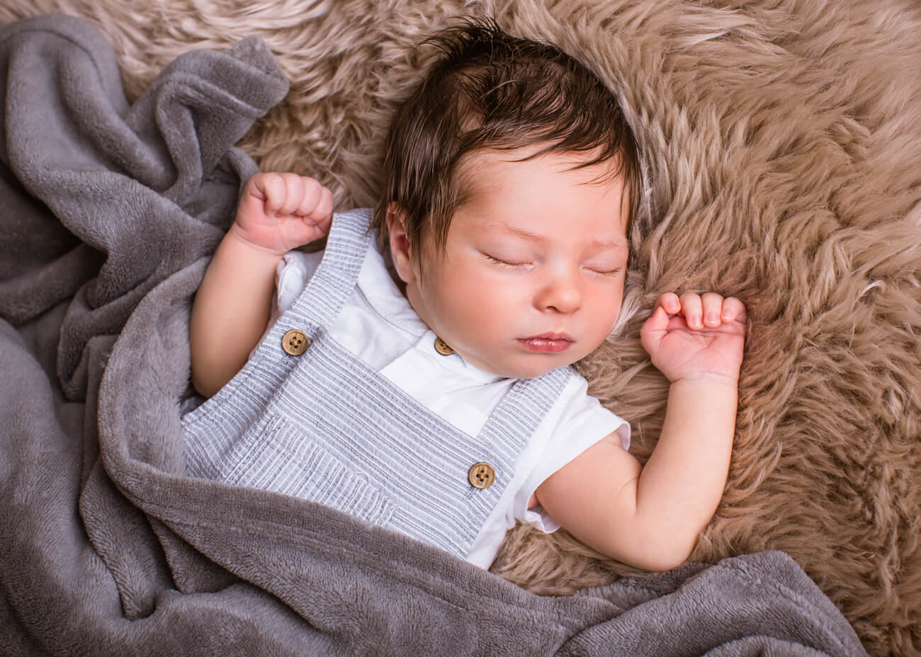 Baby mit blauer Latzhose liegt auf Felldecke 