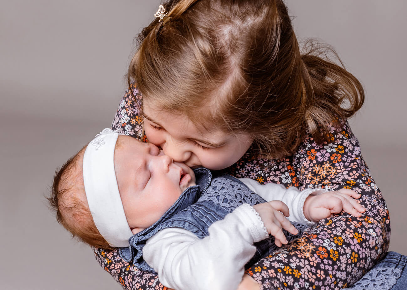 große Schwester küsst Baby im Schoß