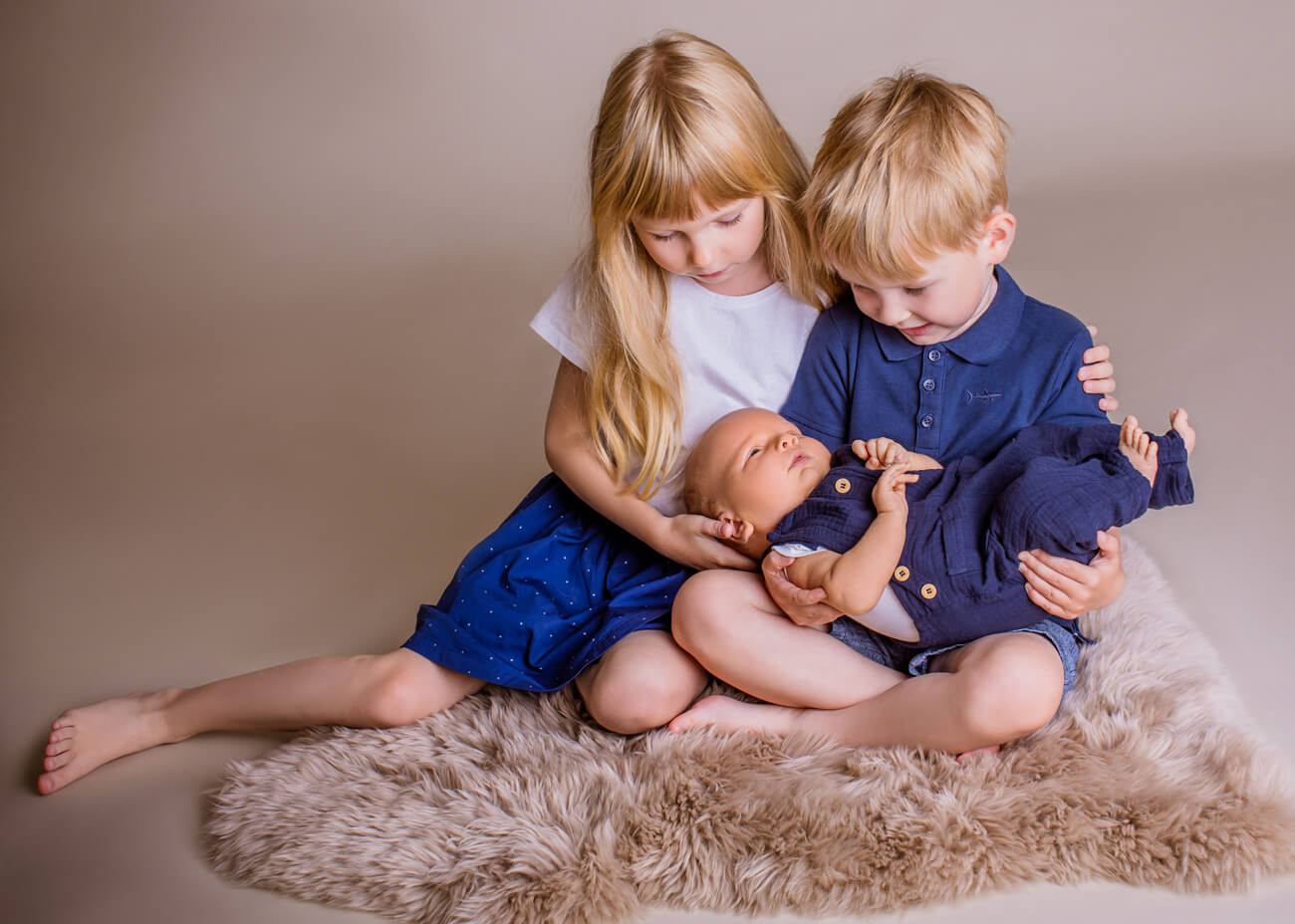 Geschwister halten kleines Baby im Arm und sehen es an