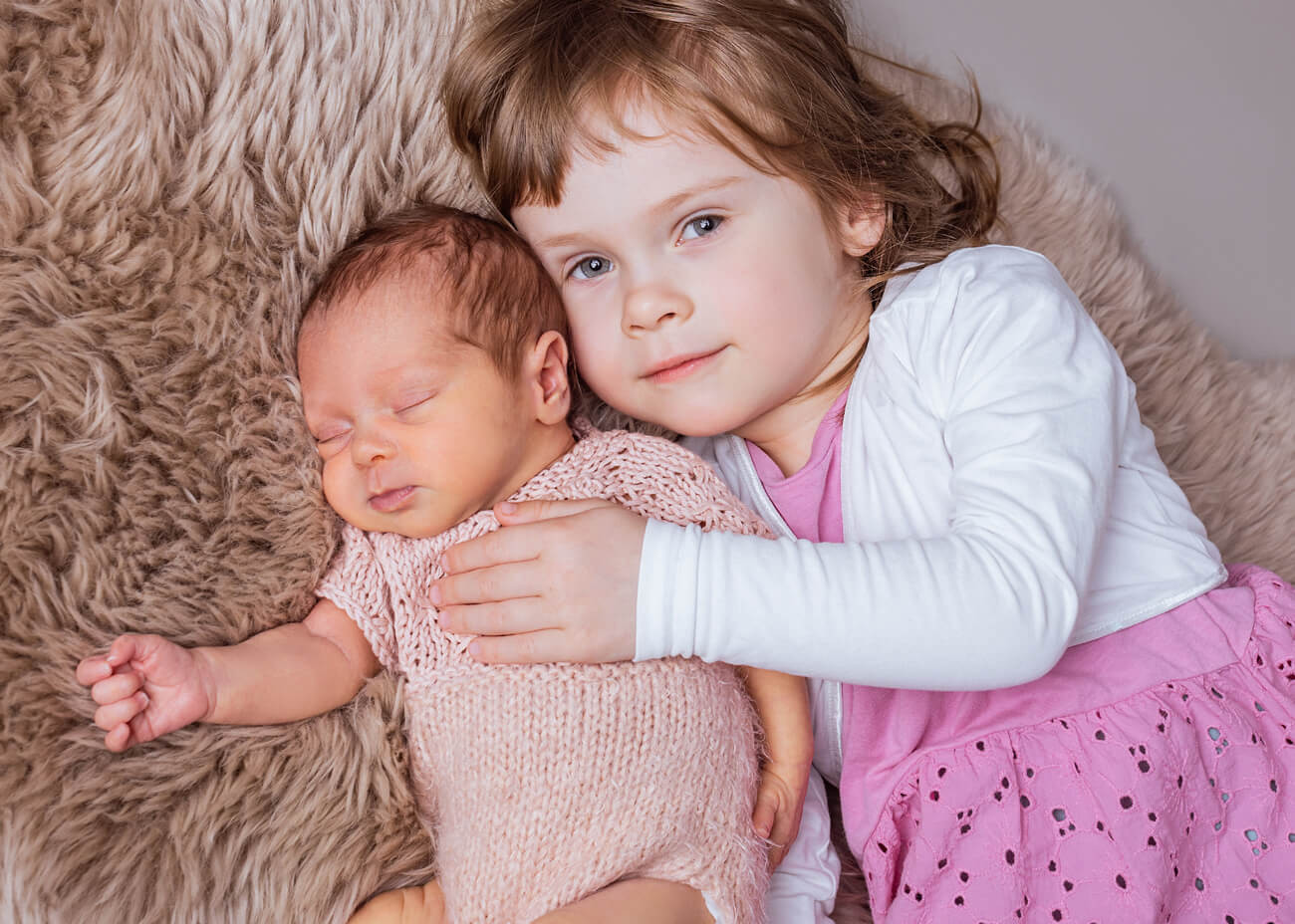 Baby liegt mit großer Schwester auf Felldecke